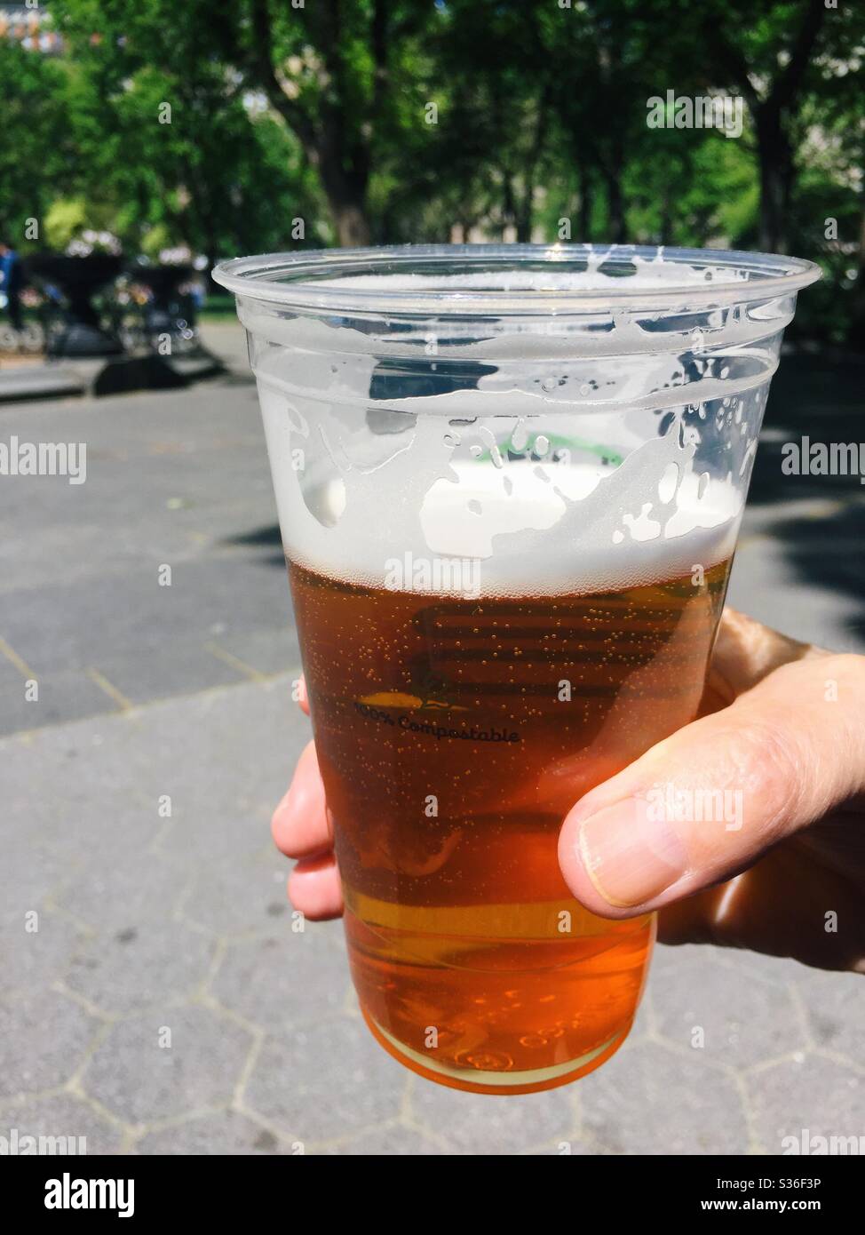 Man holding a large beer in a plastic cup in a public park, USA - Smartphone Captured Stock Image