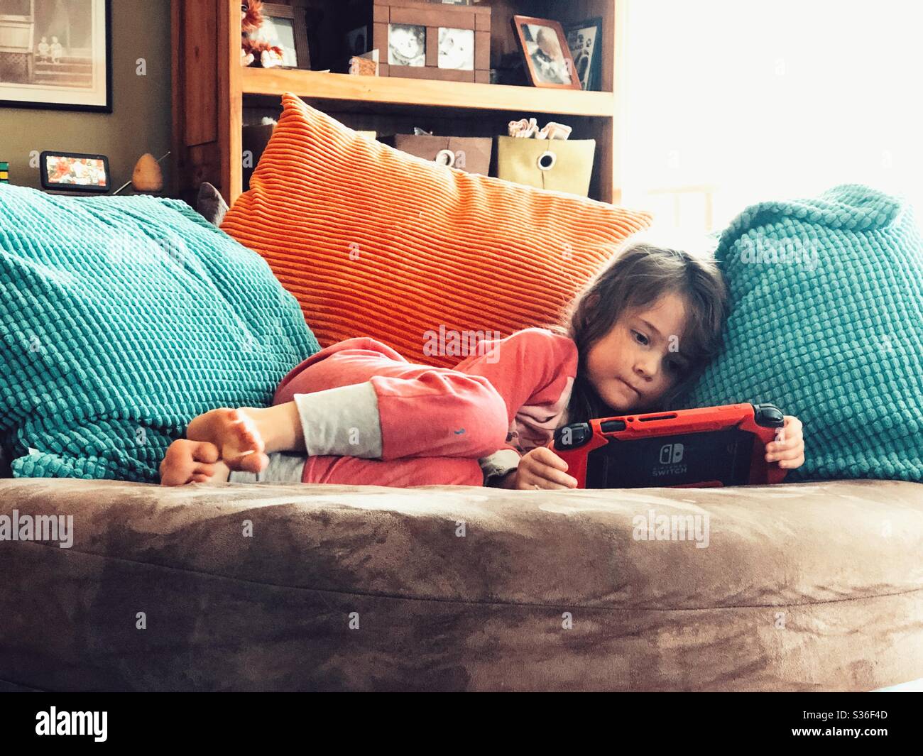 Young girl laying on chair playing Nintendo Switch Stock Photo