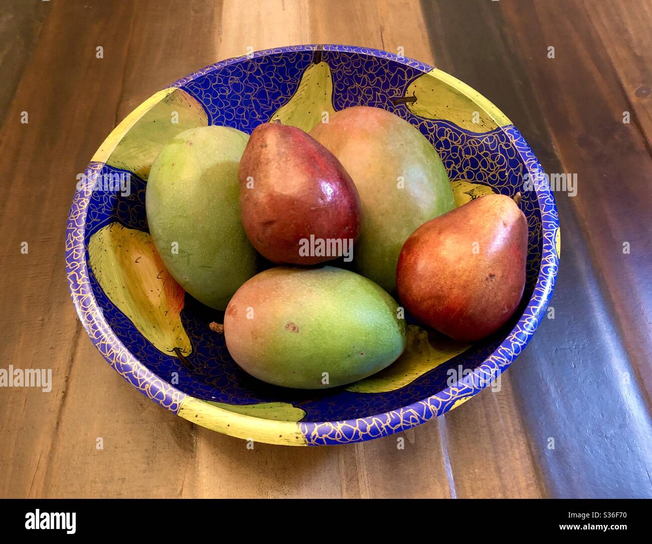 3 mangos and 2 Anjou pears in a hand painted wooden fruit bowl. - Smartphone Captured Stock Image