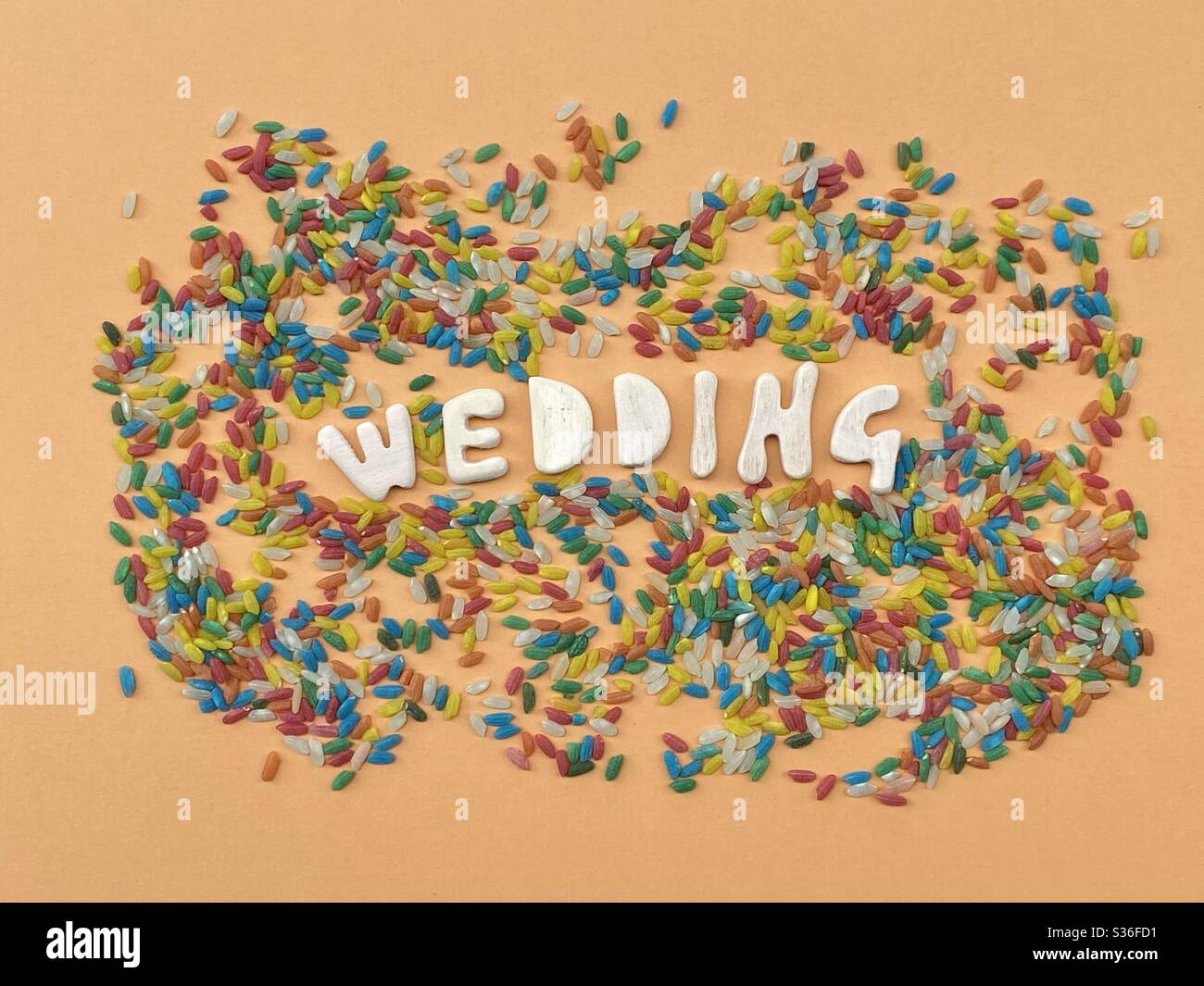 Wedding card composed with handmade wooden letters over orange color and multicolored rice - Smartphone Captured Stock Image