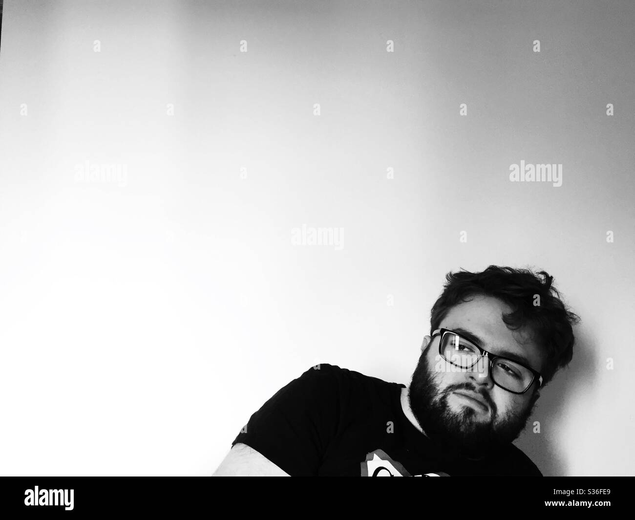 A black and white portrait of a young man with beard and glasses looking unkempt and bored whilst in self isolation during coronavirus with copy space Stock Photo