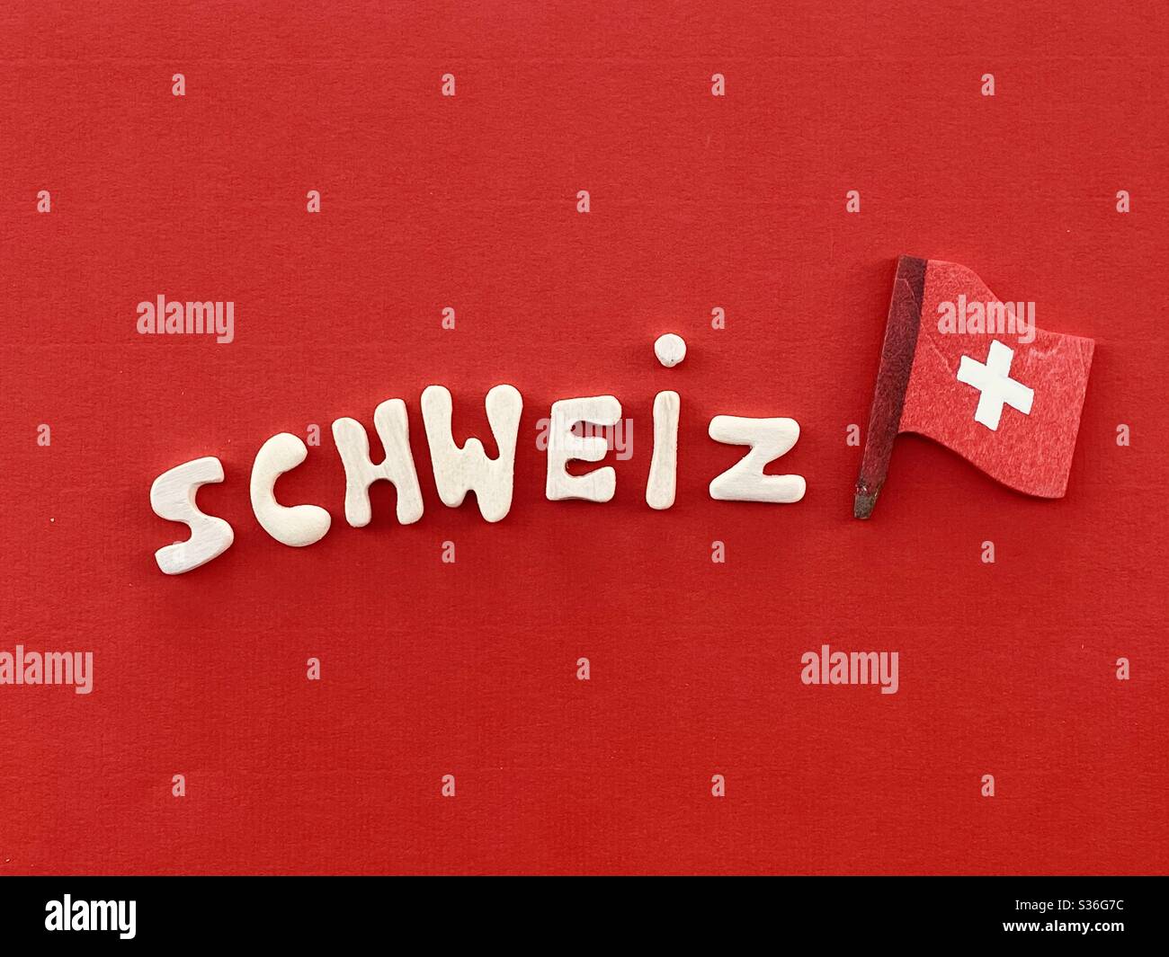 Schweiz, Switzerland country name in german language composed with handmade wooden letters over red color and wooden national flag Stock Photo