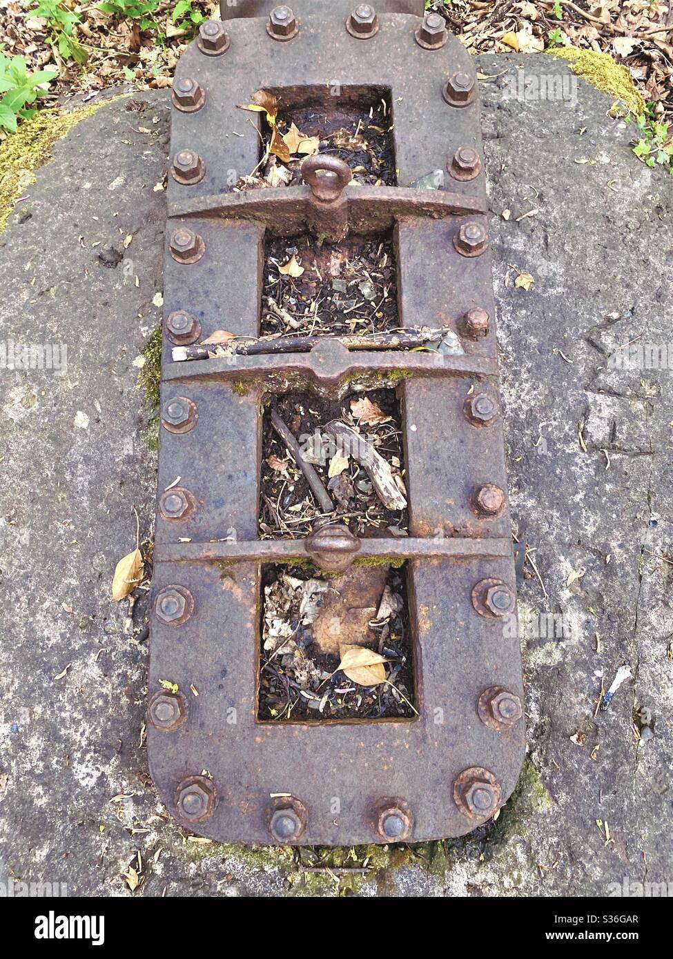 Abstract old rural sewerage infrastructure in woodland. Rusty steel pipe clamped and bolted down to concrete - Smartphone Captured Stock Image