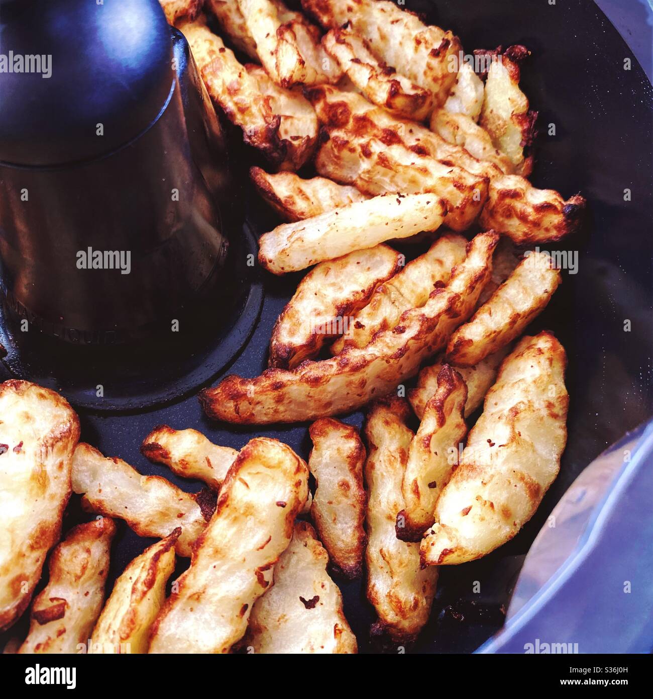 Closeup view of crinkle cut fries in the pan of a rotating air fryer. Homemade fries with a crinkle cutter fried in hot air, a healthier way of cooking. Crispy potato chips for dinner. - Smartphone Captured Stock Image