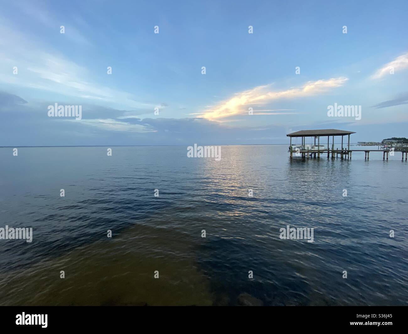 Perspective evening skies with sun reflecting into clouds and boat dock on bay water - Smartphone Captured Stock Image