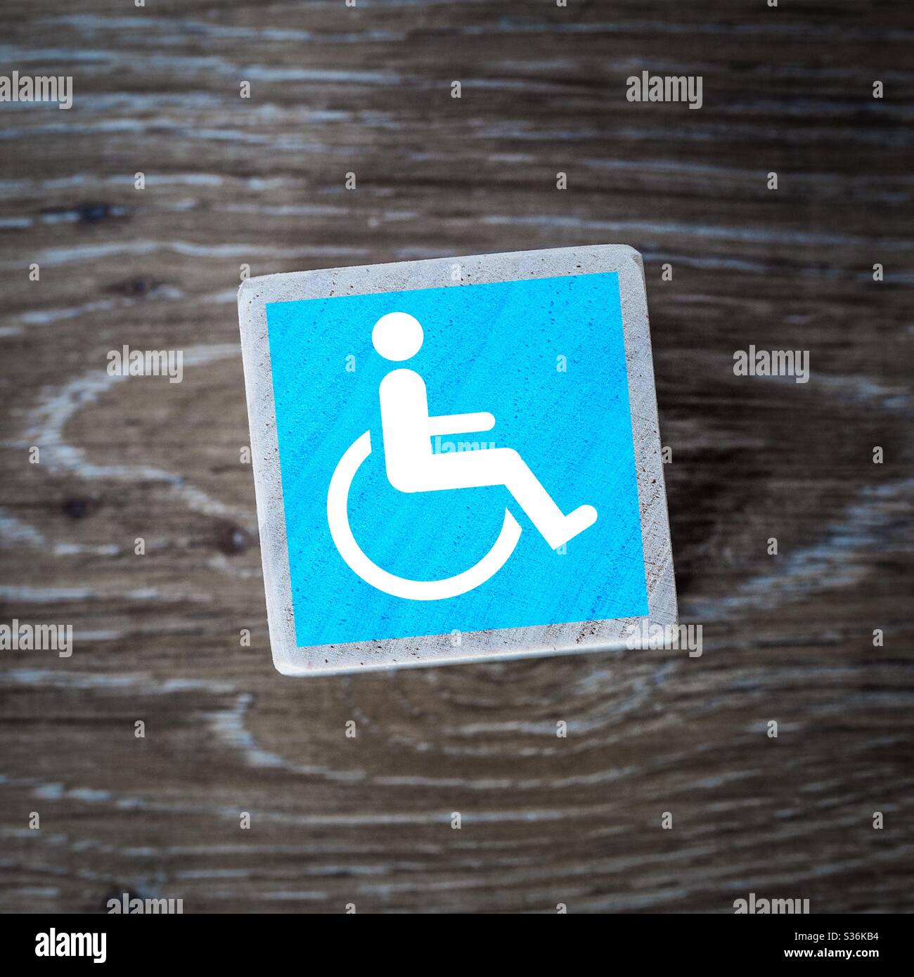 A blue disability or disabled wheelchair icon sign or symbol on a wooden block background with copy space - Smartphone Captured Stock Image