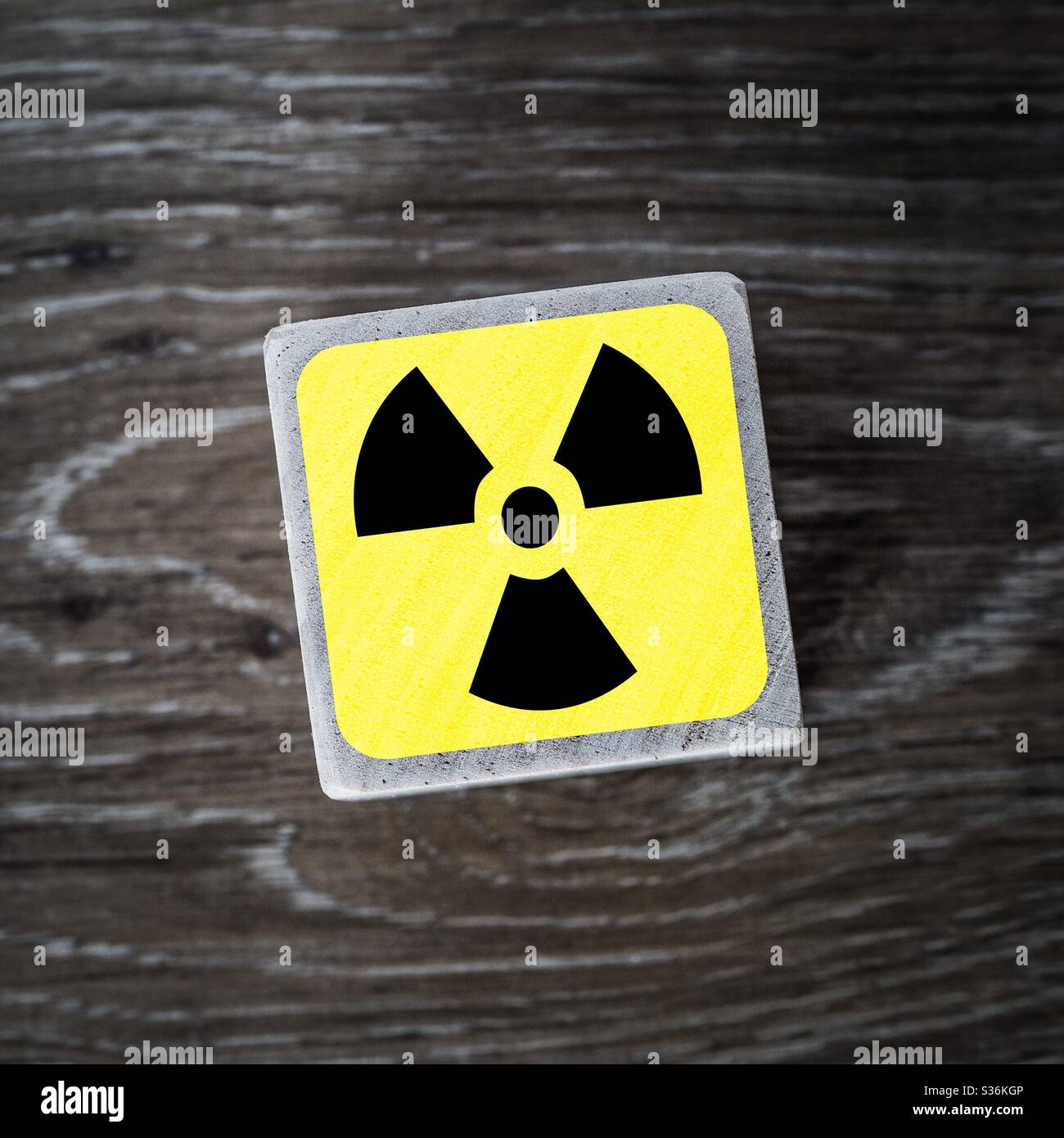 A radioactive or radiation warning sign on a yellow square with a wooden background - Smartphone Captured Stock Image