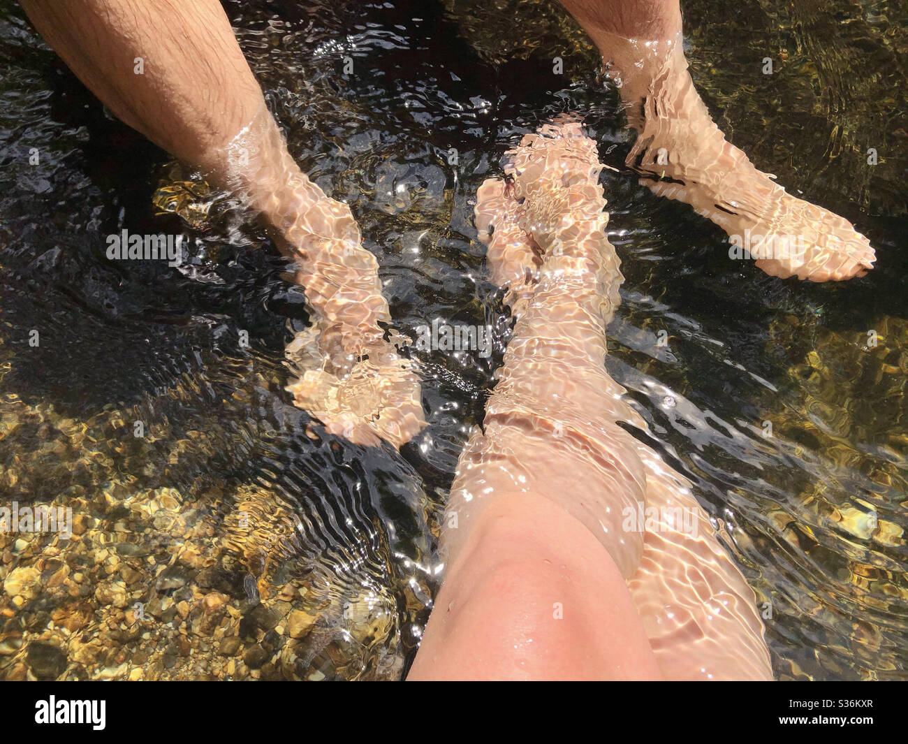 Man and woman relaxing at mountain swimming hole with feet in water in the summer time - Smartphone Captured Stock Image