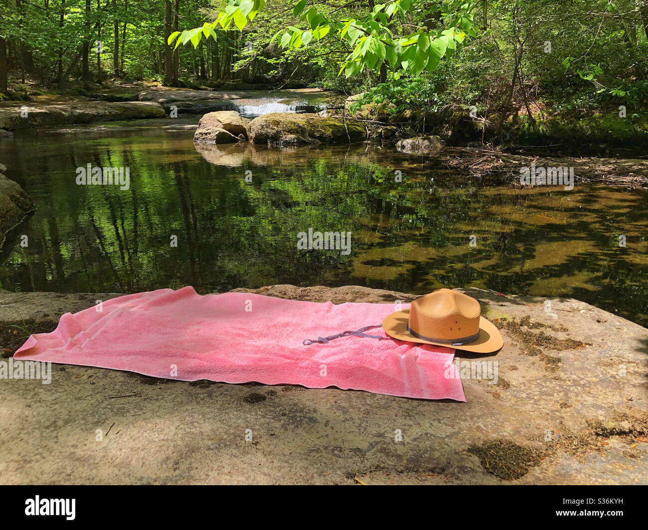 Summer straw hat and pink towel of woman relaxing by lake in the the mountains in the summer - Smartphone Captured Stock Image