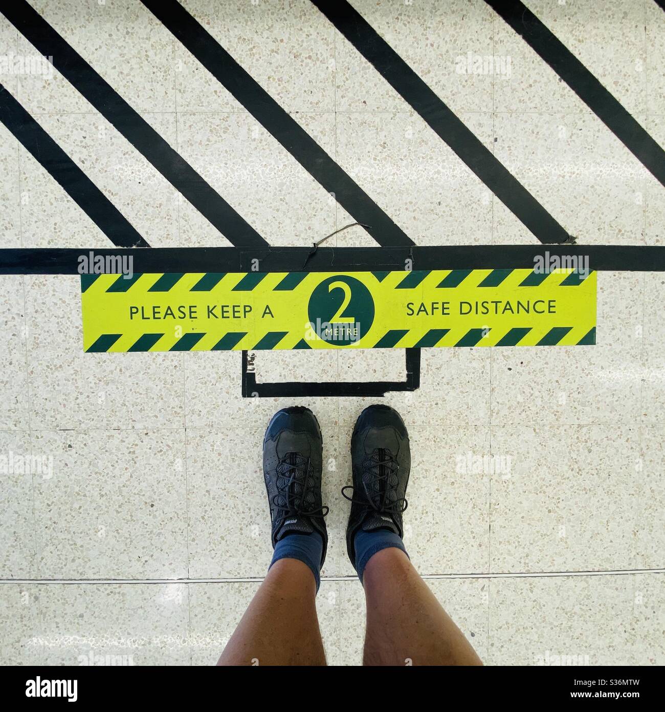 Looking down at a pair of feet standing next to social distancing signs on the floor of a supermarket during the coronavirus crisis in the UK - Smartphone Captured Stock Image