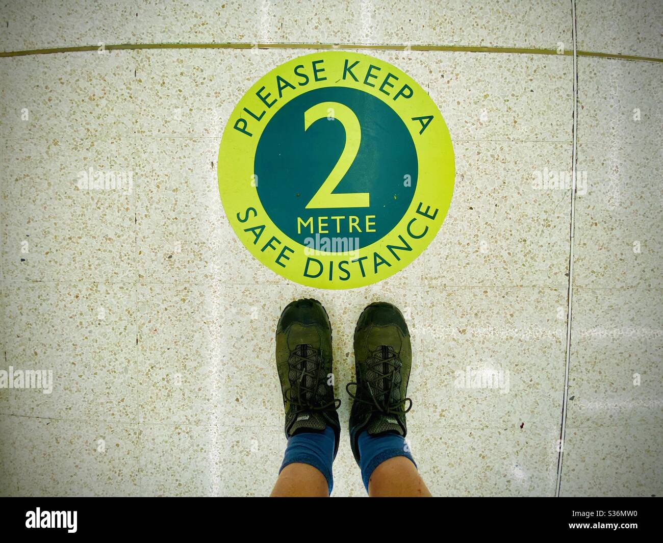Looking down at a pair of feet standing next to a circular social distancing sign in a UK supermarket during the coronavirus crisis - Smartphone Captured Stock Image