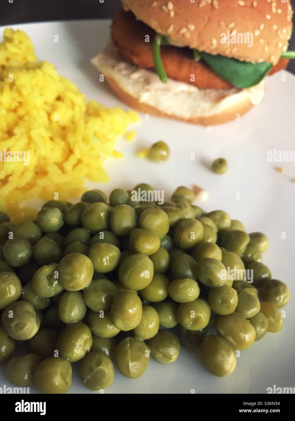 Close up of a chicken cutlet sandwich accompanied by servings  of sweet peas and yellow rice - Smartphone Captured Stock Image