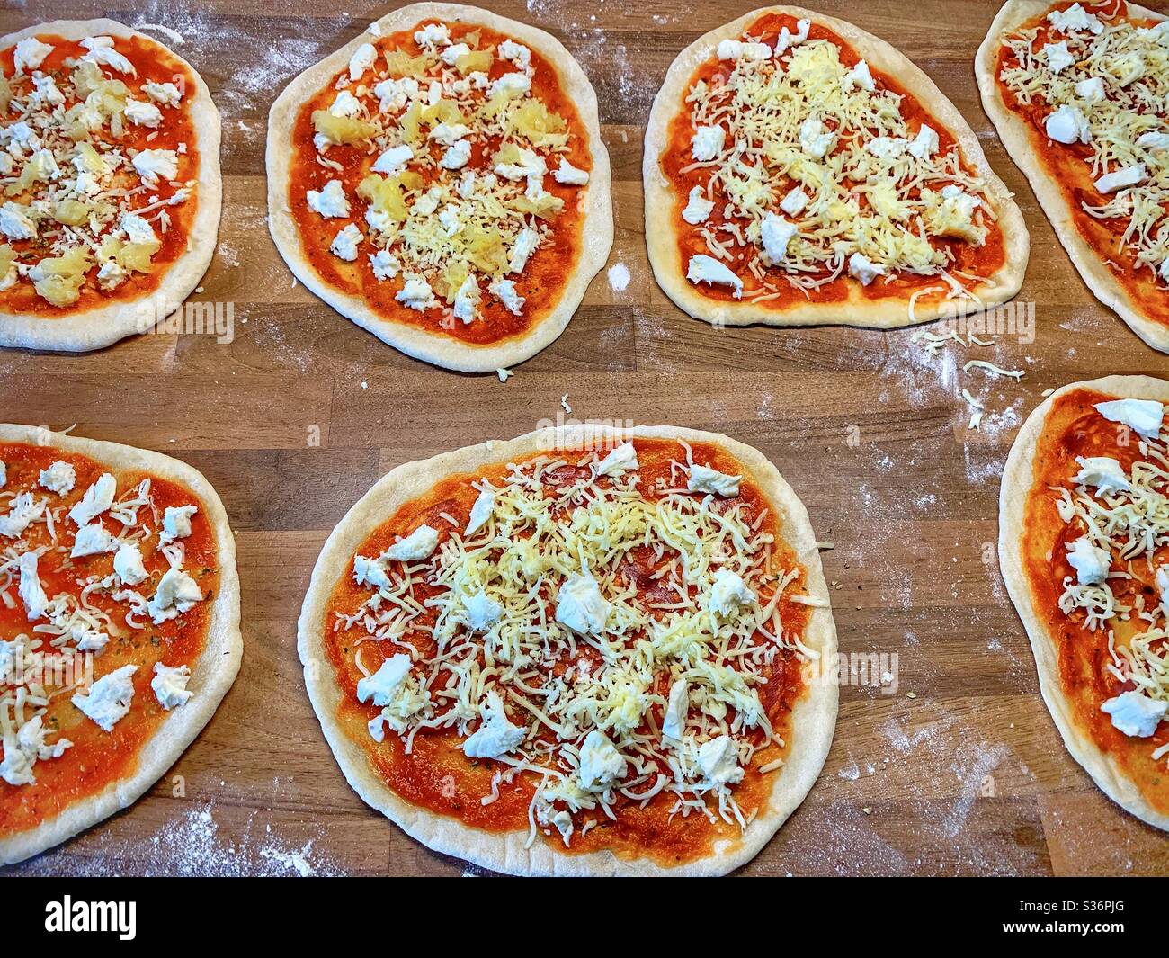 Seven uncooked homemade pizzas ready to go into the oven. On a floured walnut wood butchers block. Stock Photo