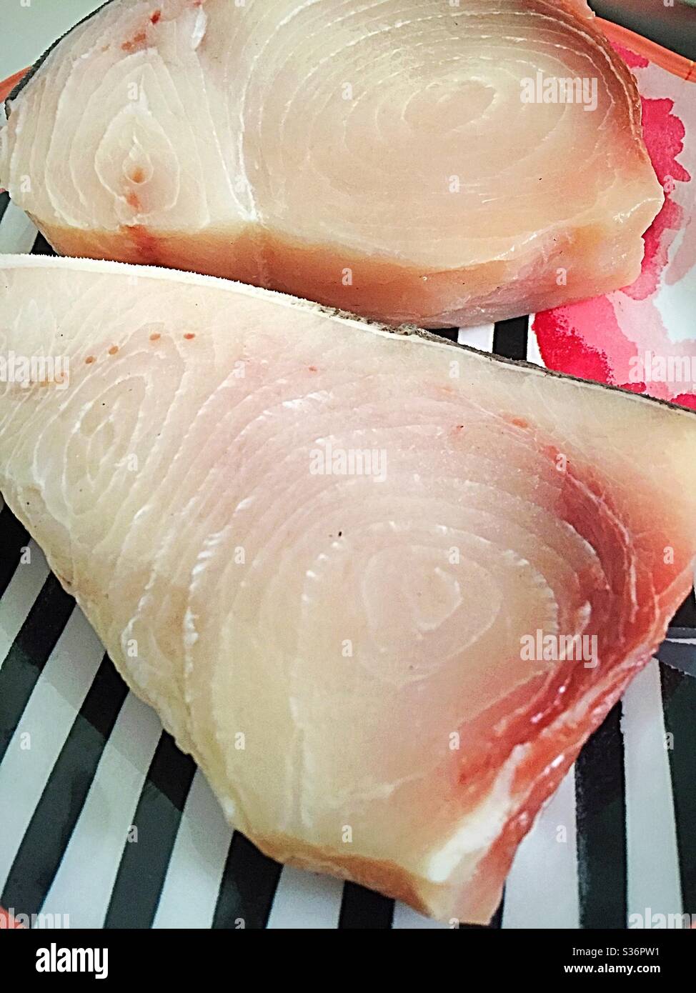 Close up of two fresh raw swordfish steaks on a black and white striped plate - Smartphone Captured Stock Image