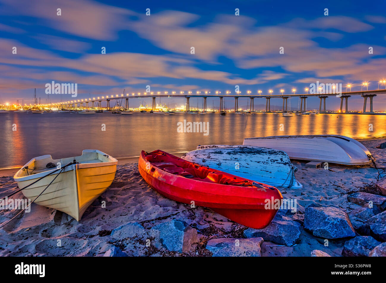 Colorful dinghy boats in the foreground with the Coronado Bay bridge in the distance under a cloudy twilight sky Stock Photo