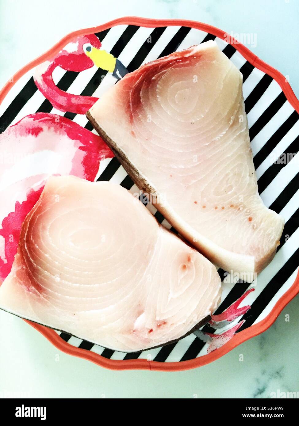 Close up of two fresh swordfish steaks on a Kitch flamingo plate, USA - Smartphone Captured Stock Image