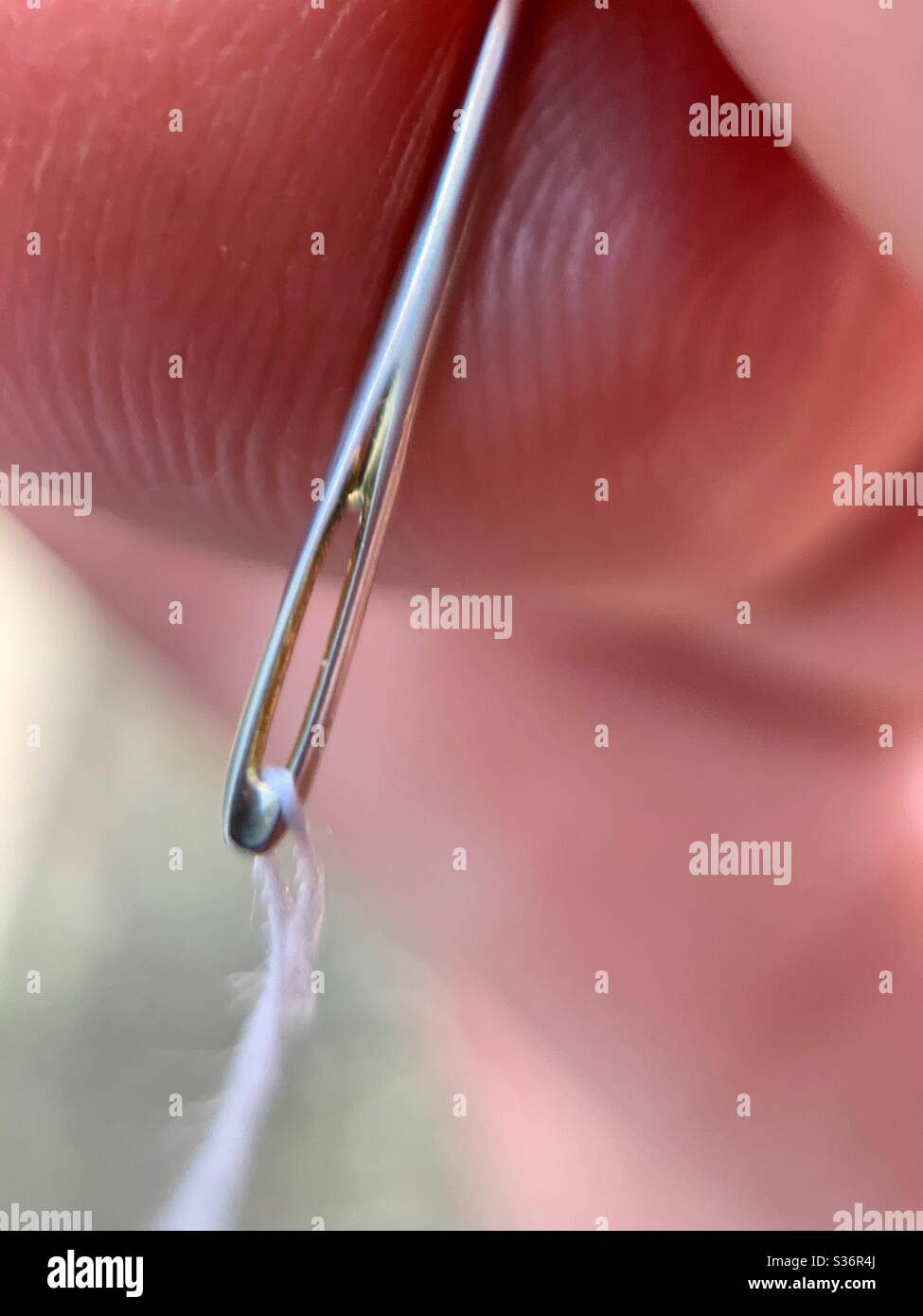 Fingers holding a sewing needle threaded with white thread - Smartphone Captured Stock Image