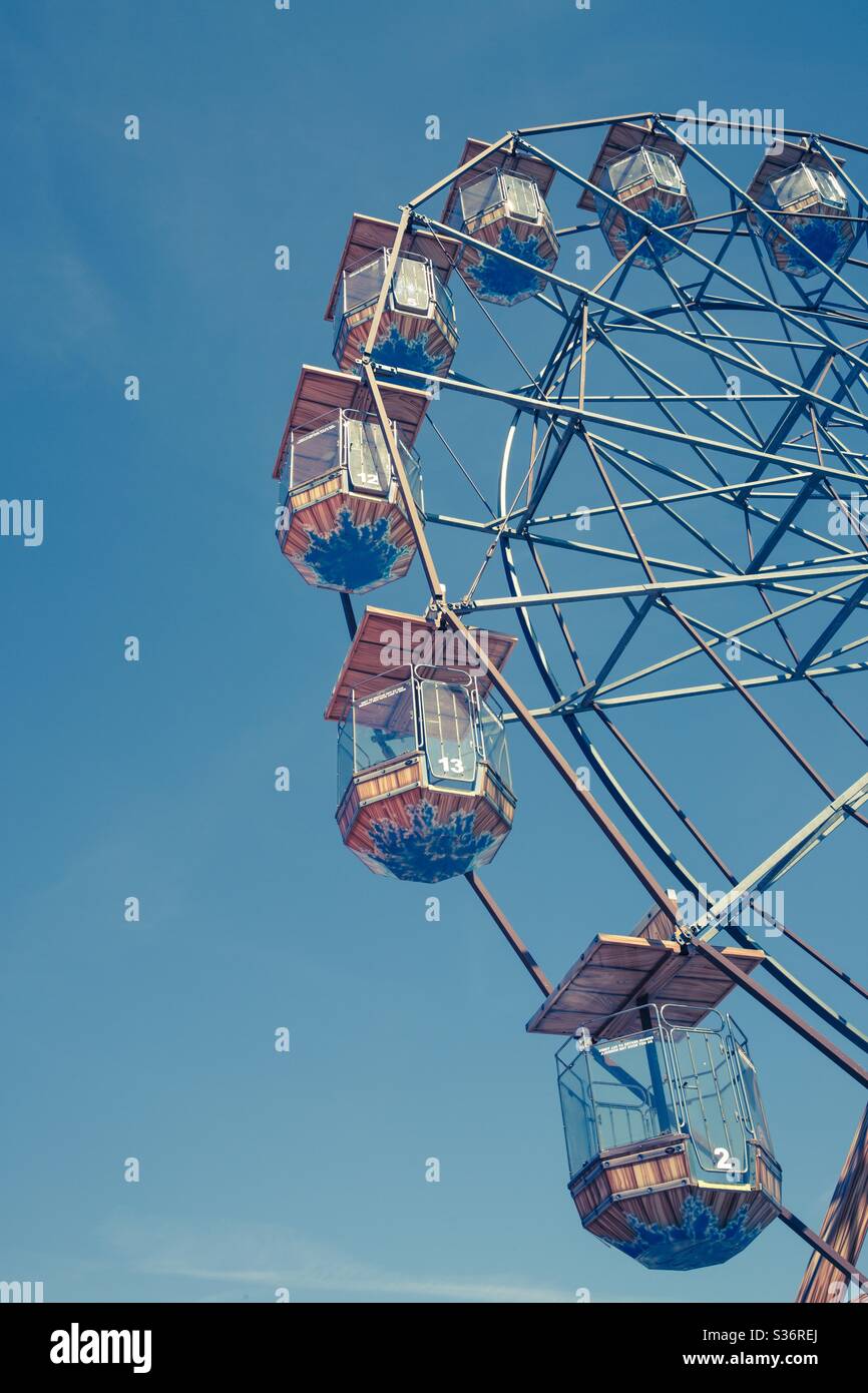 A close up low angle view of the suspended seats of a Ferris Wheel at a fairground under a clear blue sky - Smartphone Captured Stock Image