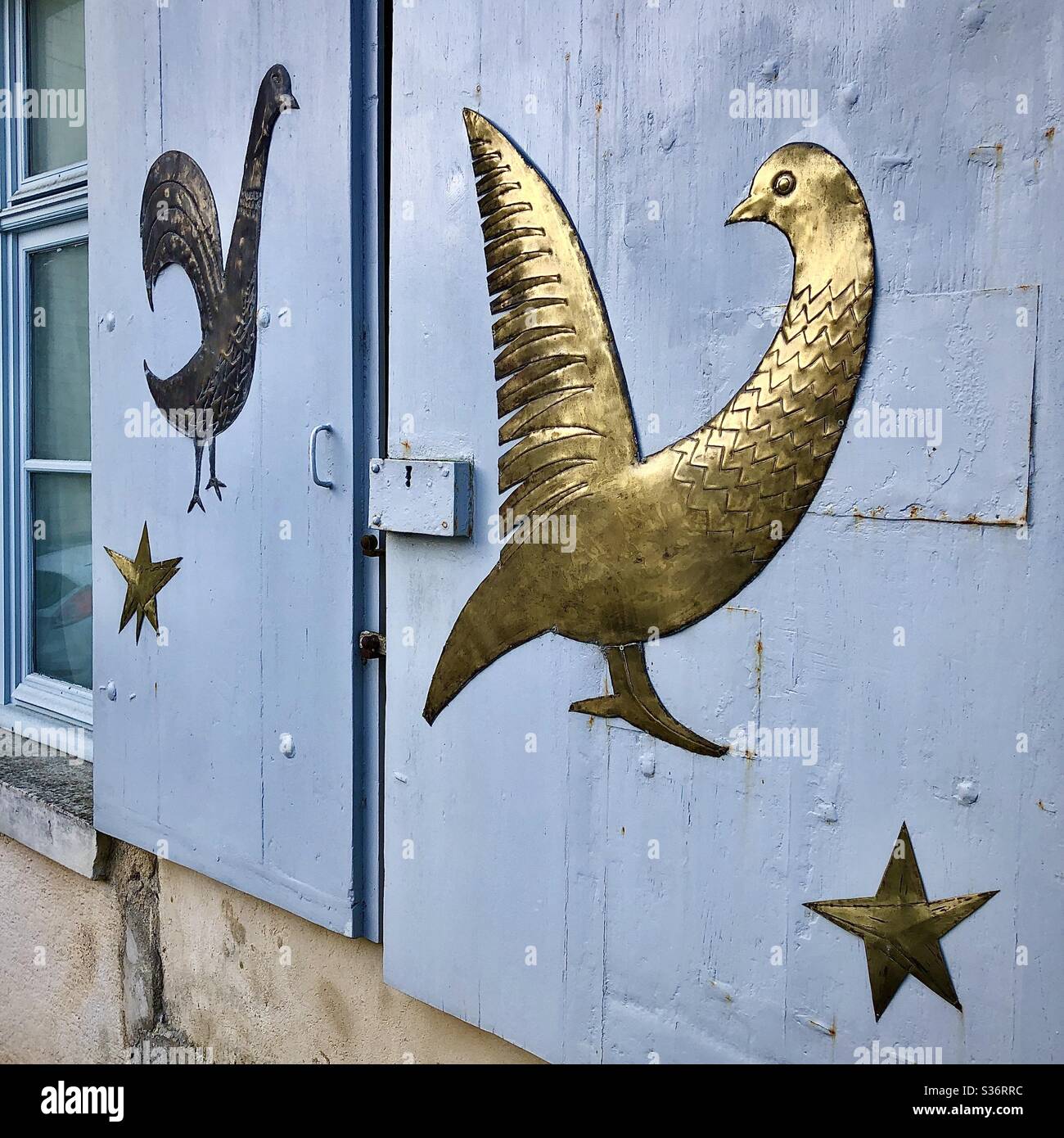 Hand-made brass shapes representing fantastic birds on window shutters - France. Stock Photo