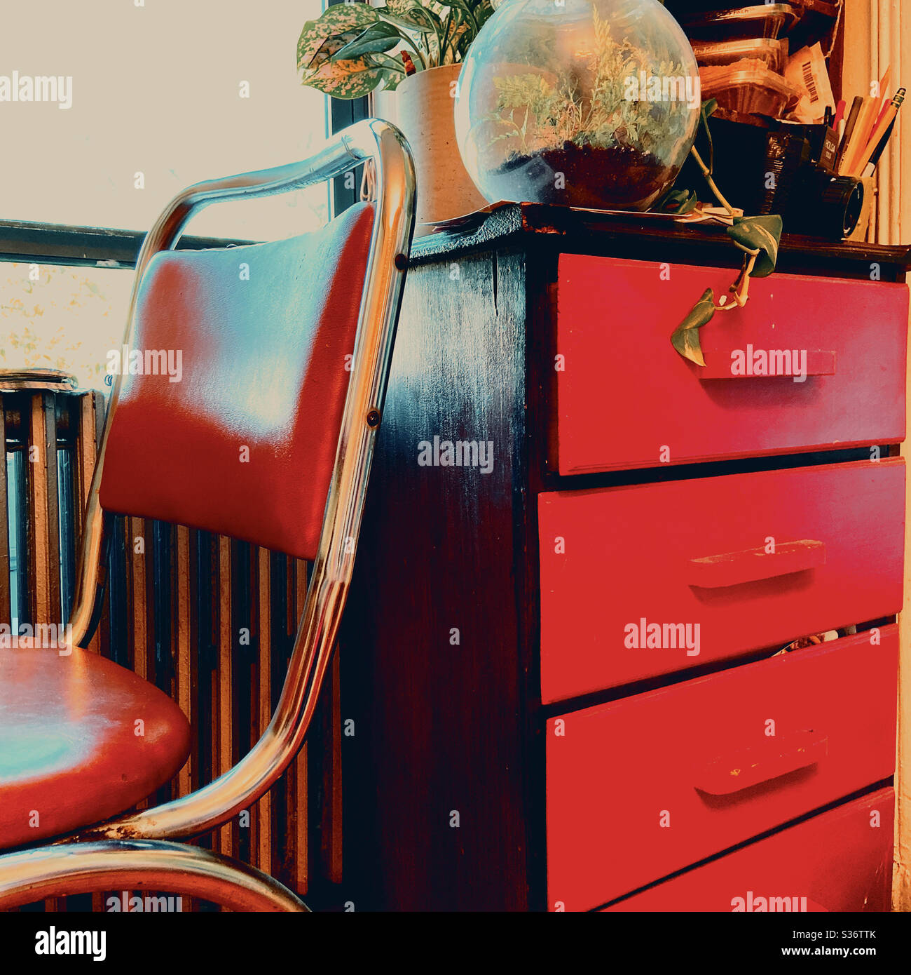 A red chair next to a red chest of drawers with plants Stock Photo