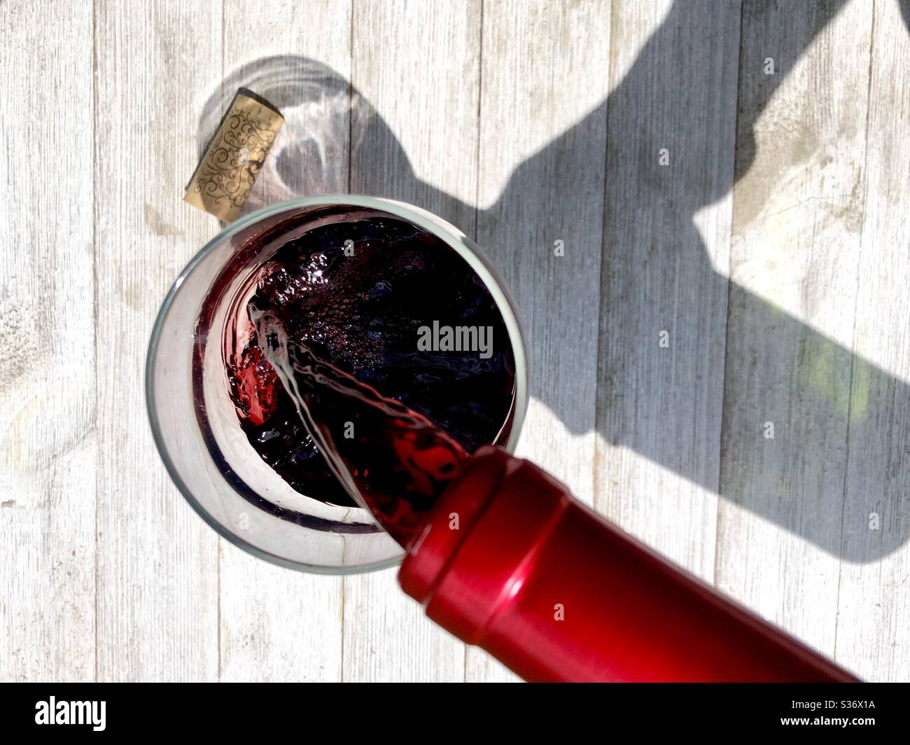 Red wine being poured into a glass on a wooden surface in natural sunlight - Smartphone Captured Stock Image