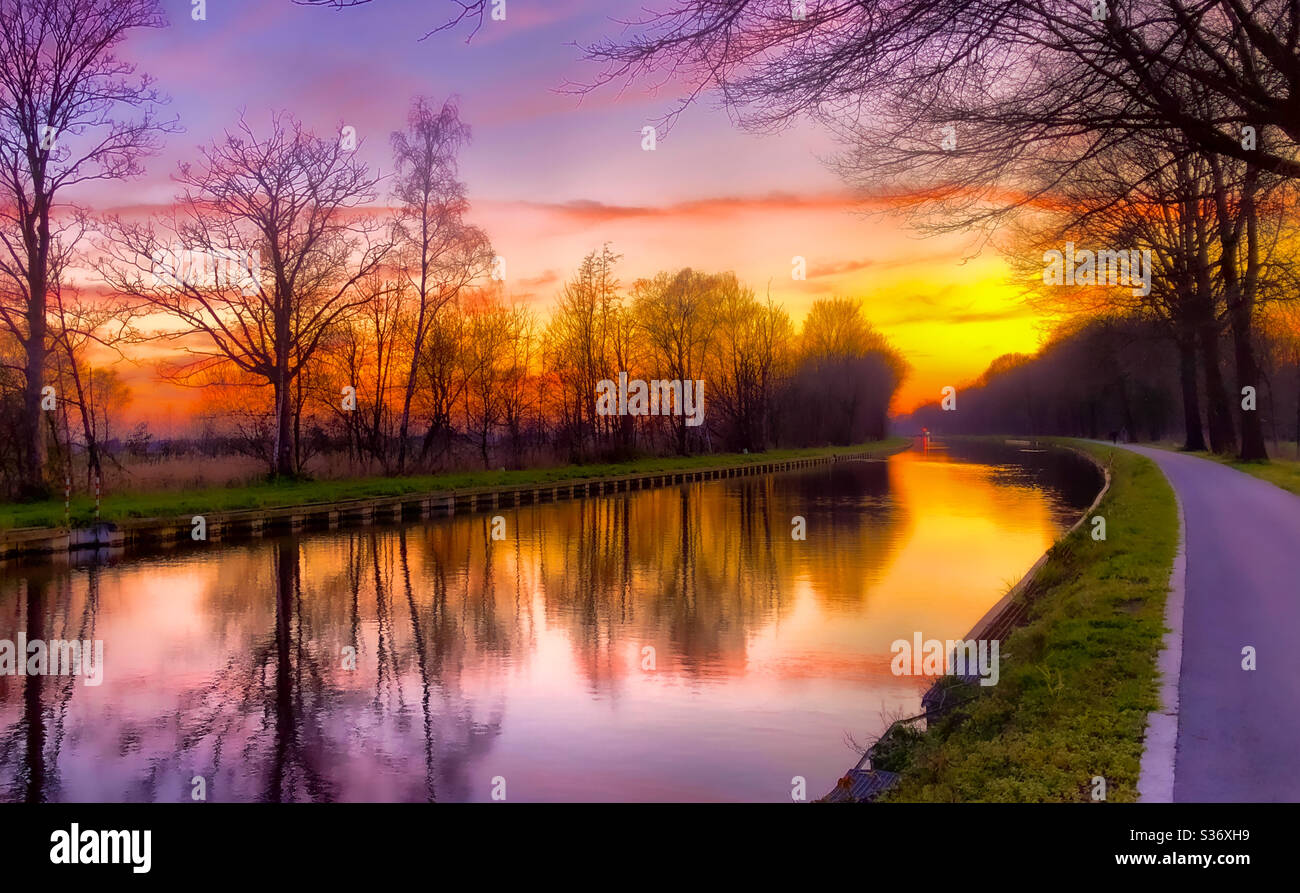 Dramatic and colorful sunset reflected on the water of the canal through the woods - Smartphone Captured Stock Image
