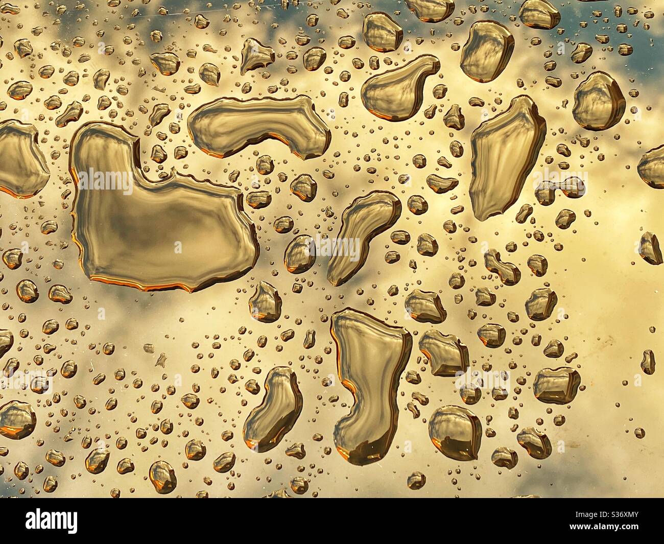 Globules of water standing on a glass table top with a reflection of clouds in the sky - Smartphone Captured Stock Image