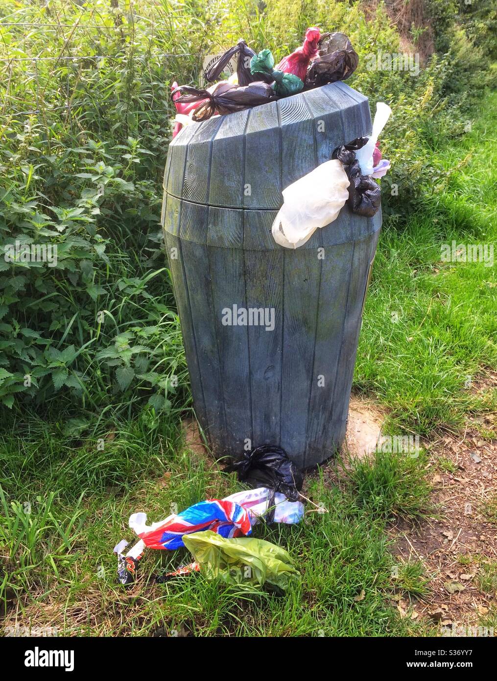 Overflowing park waste bin with dog poo bags on the floor. - Smartphone Captured Stock Image