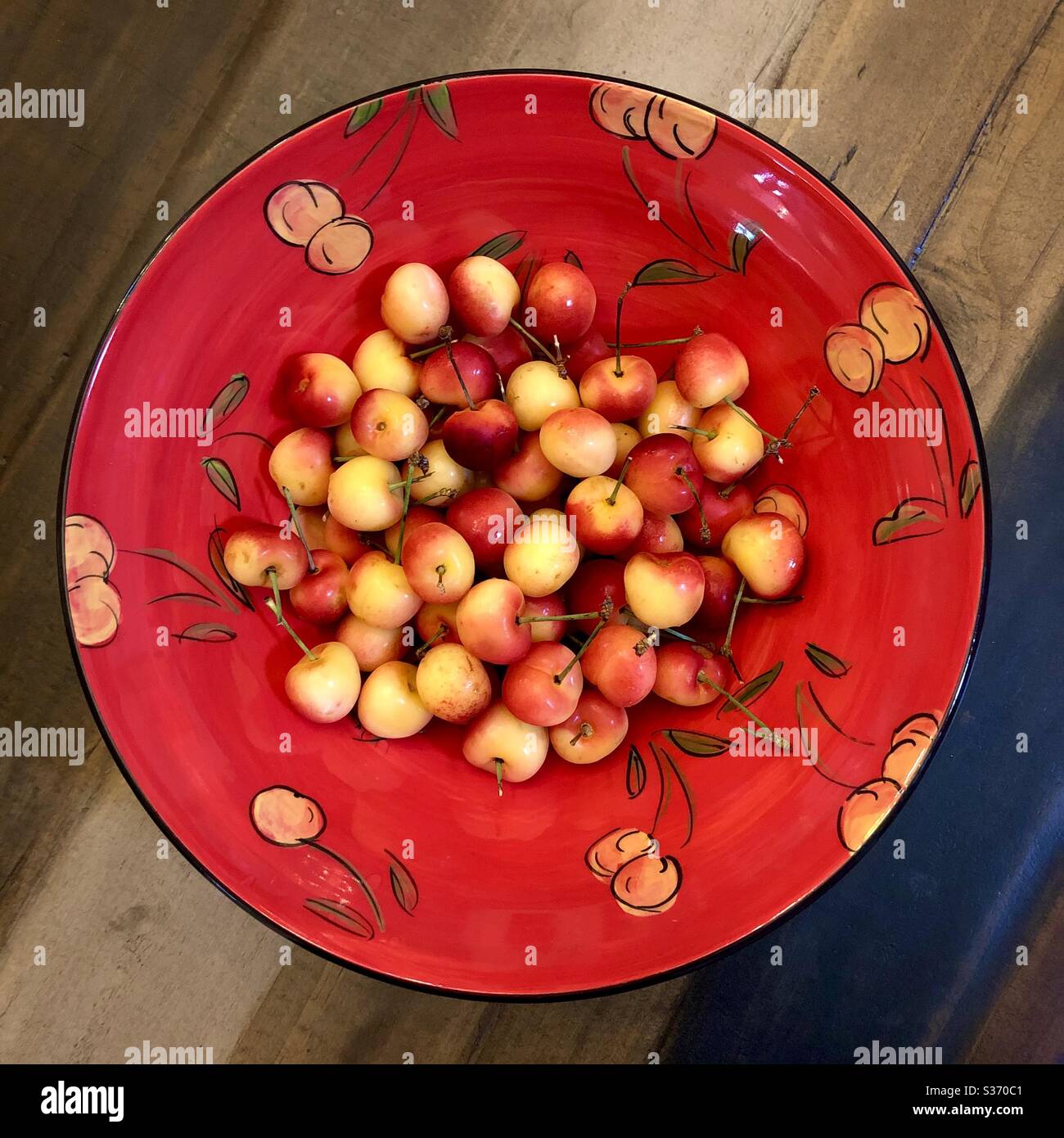 Overview of a bowl of rainier cherries in a handpainted ceramic bowl with a rainier cherry motif. Stock Photo