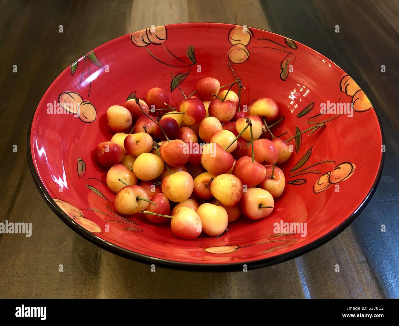 A bowl of rainier cherries in a ceramic bowl painted with a rainier cherry motif. Stock Photo