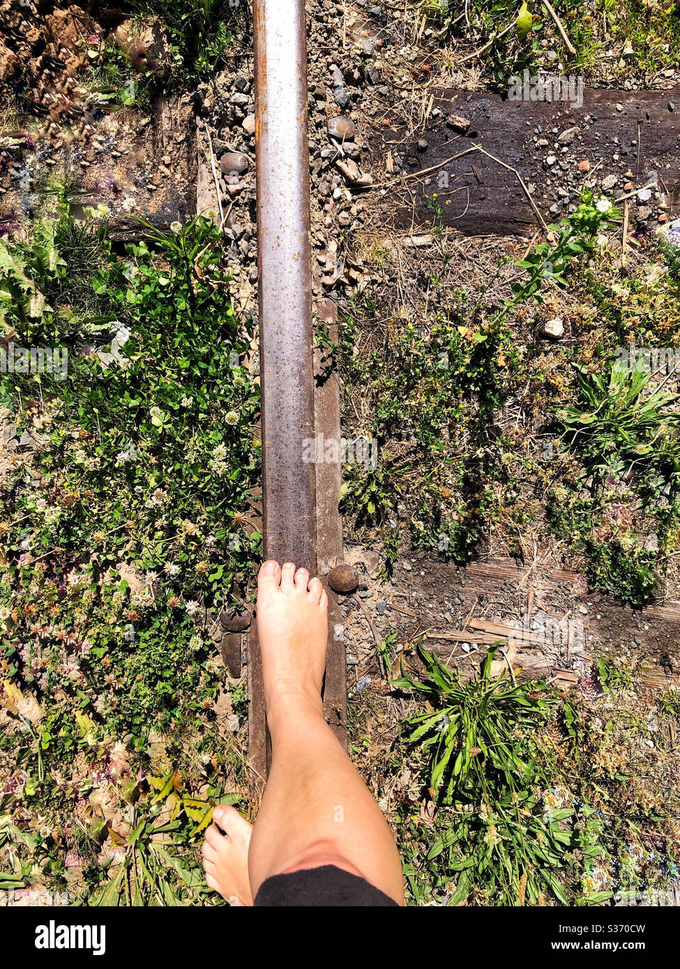 Woman walking on abandoned rail road tracks, barefoot in the summer, balancing on one rail Stock Photo