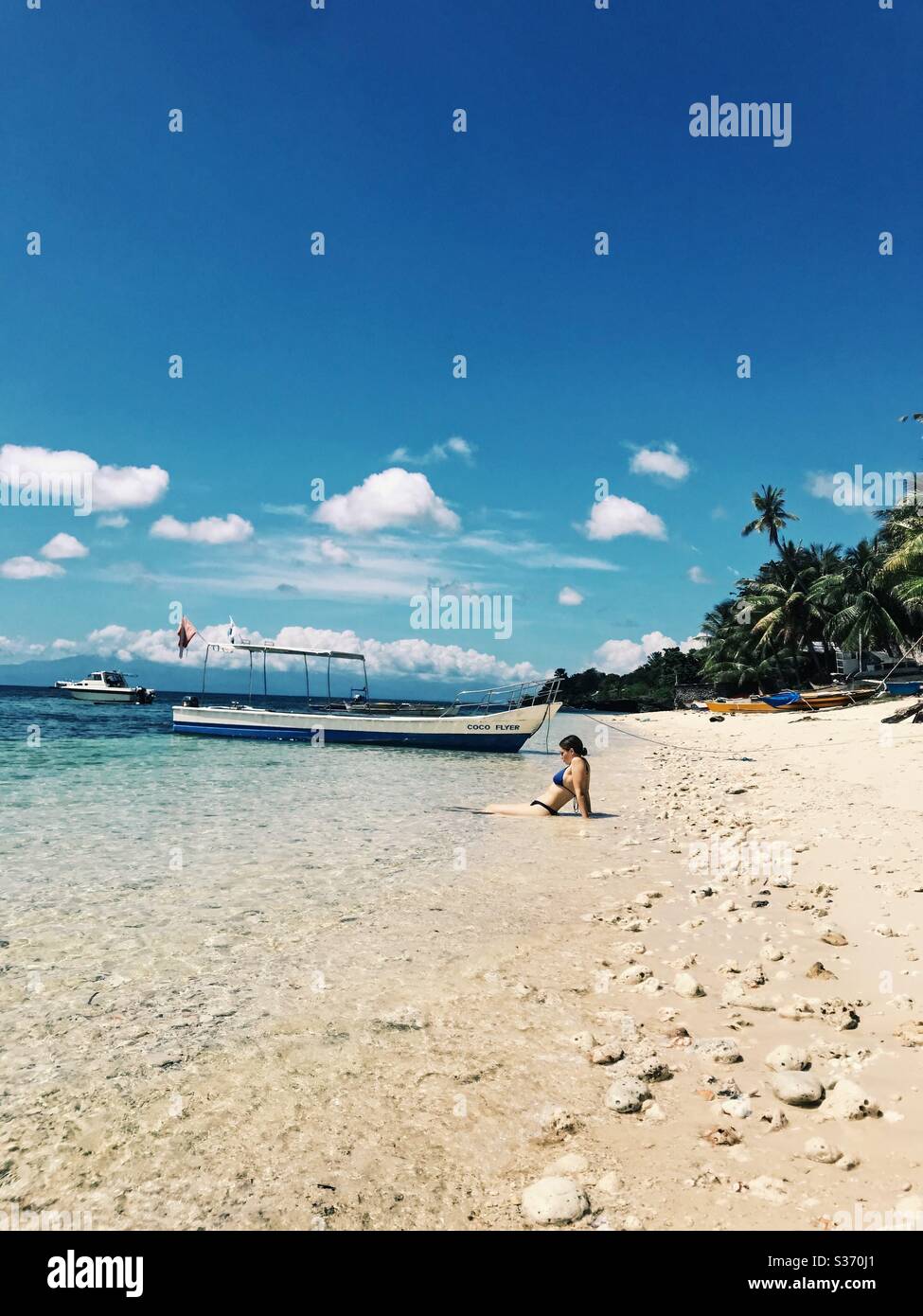 Woman in a bikini sits in shallow sea on exotic beach in San Juan, Siquijor, Philippines. Stock Photo