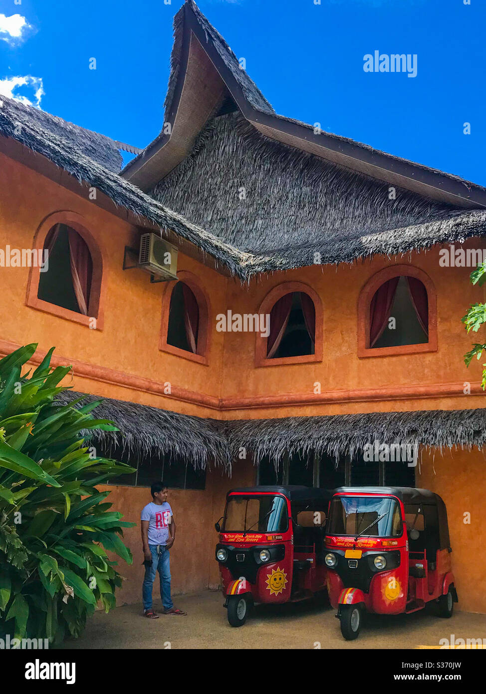Man stands next to two tricycles in front of an orange building in Siquijor, Philippines. Stock Photo