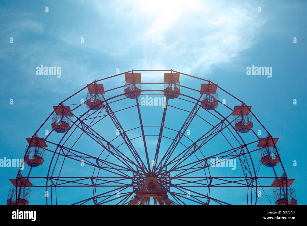 A ferris wheel or big wheel at a seaside fairground showing the symmetrical shape against the blue sky - Smartphone Captured Stock Image