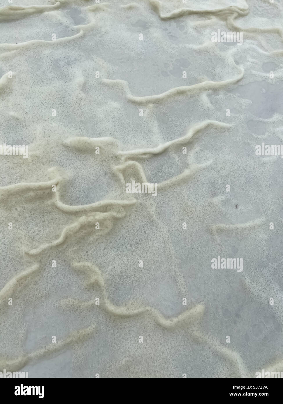 Abstract background of yellow foam blown onto beach sand from ocean water - Smartphone Captured Stock Image