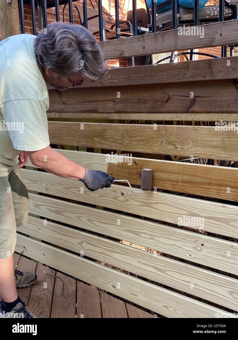 One man staining deck boards with roller Stock Photo