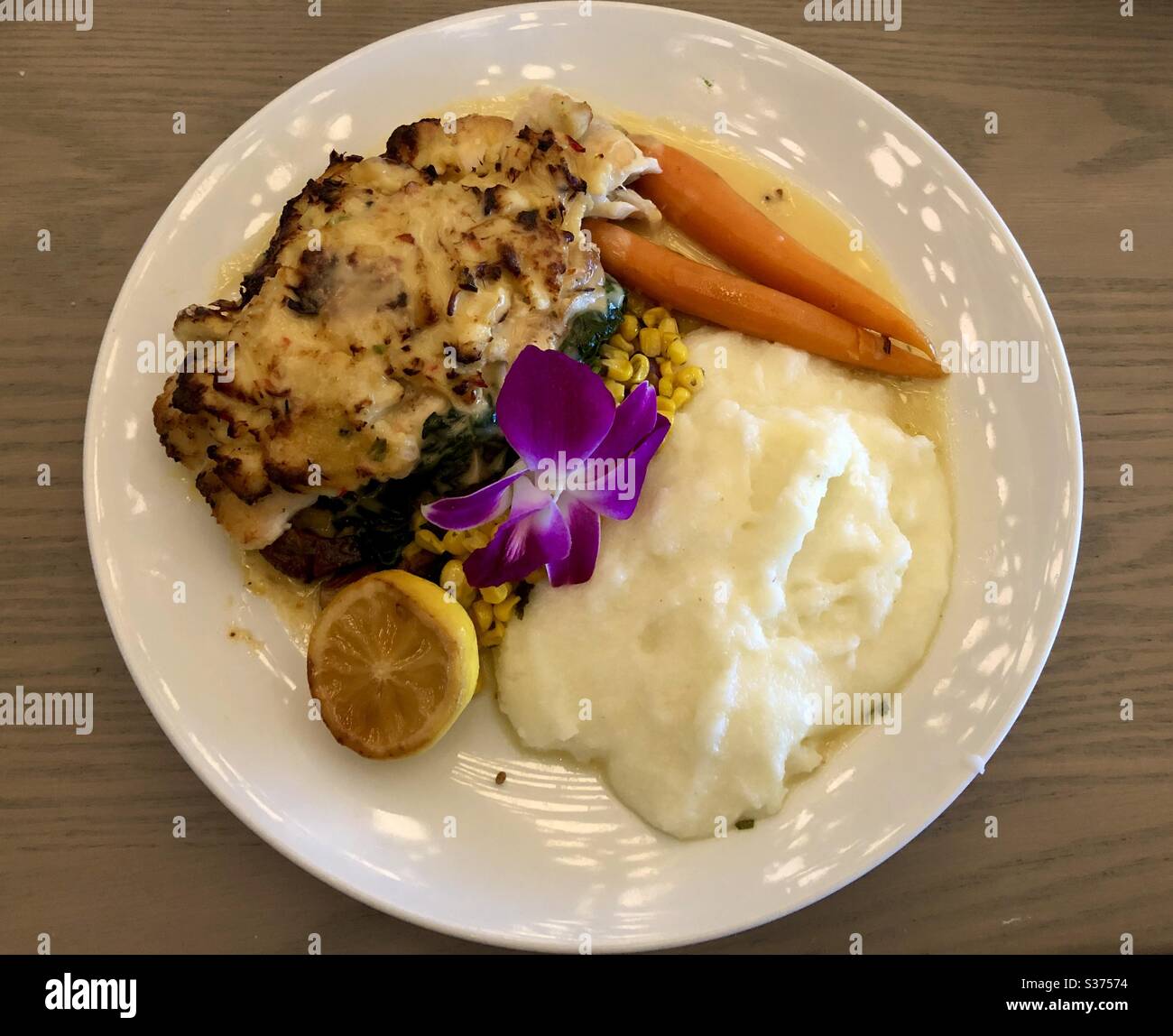 Dinner plate of crab encrusted Grouper with mashed potatoes, vegetables, lemon and an orchid garnish. - Smartphone Captured Stock Image