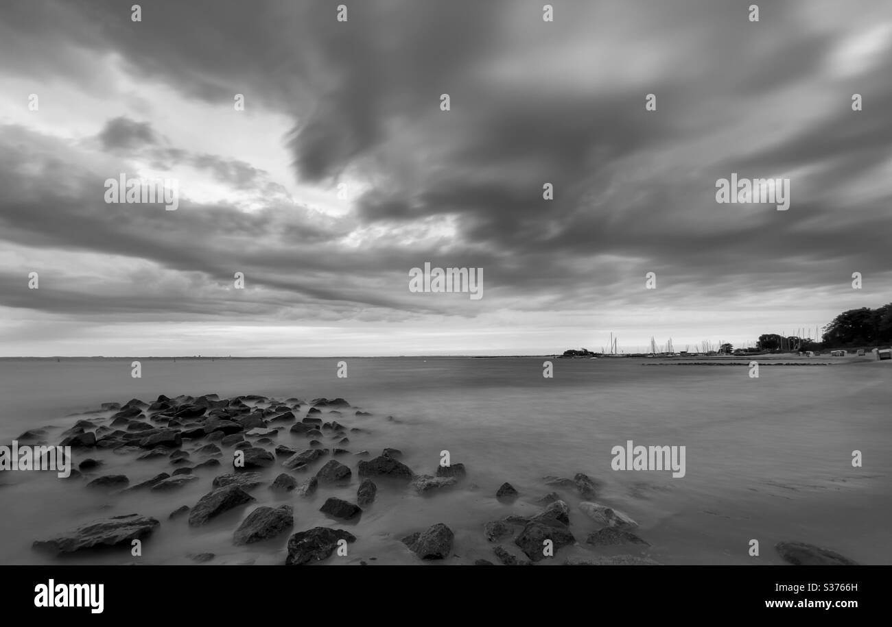 Black and white long exposure of sea waves with stones in foreground under dramatic sky, Germany - Smartphone Captured Stock Image Black and white long exposure of sea waves with stones in foreground under dramatic sky, Germany - Smartphone Captured Stock Image