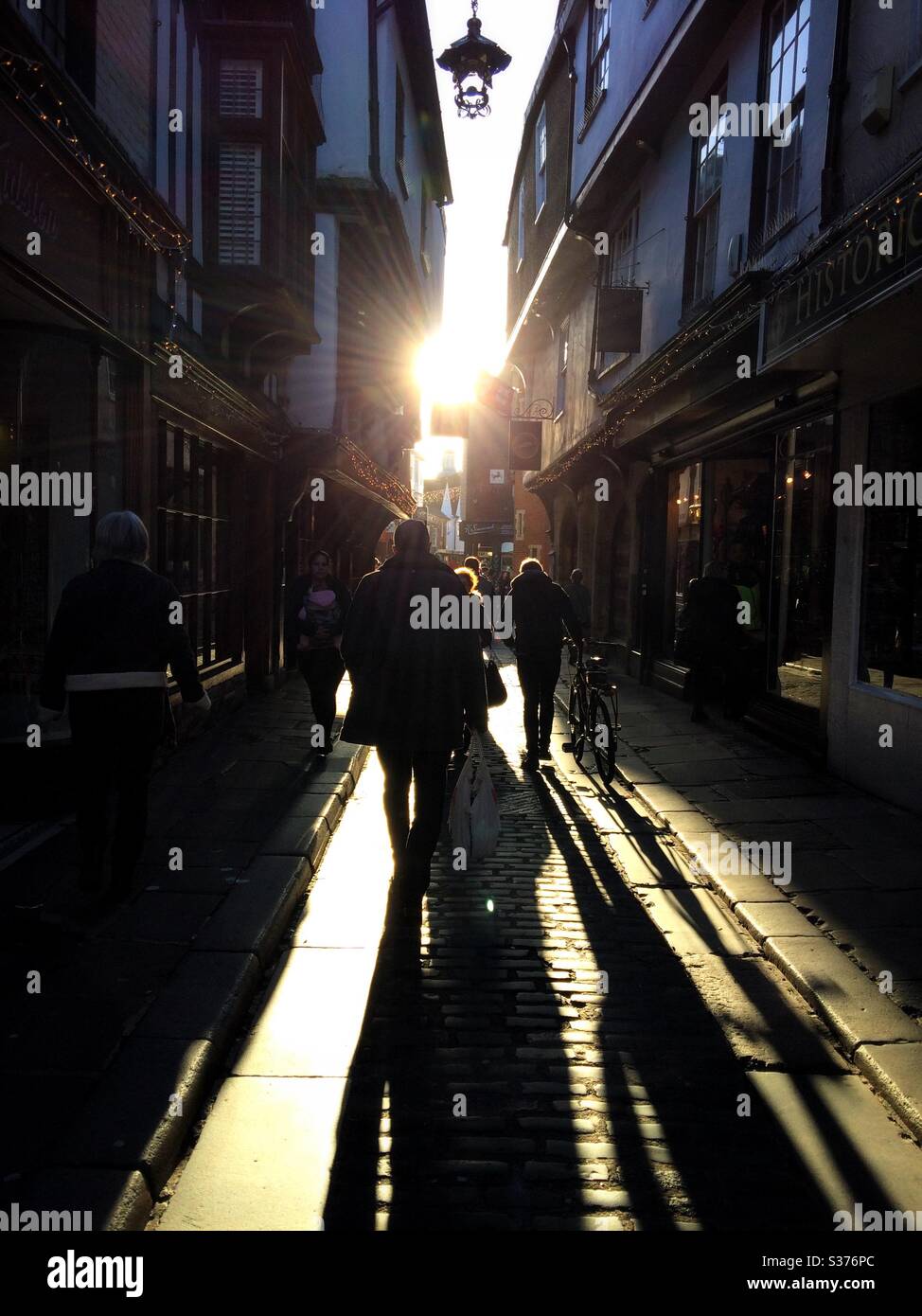 People walking along a cobbled street towards the setting sun creating long shadows in Canterbury UK - Smartphone Captured Stock Image