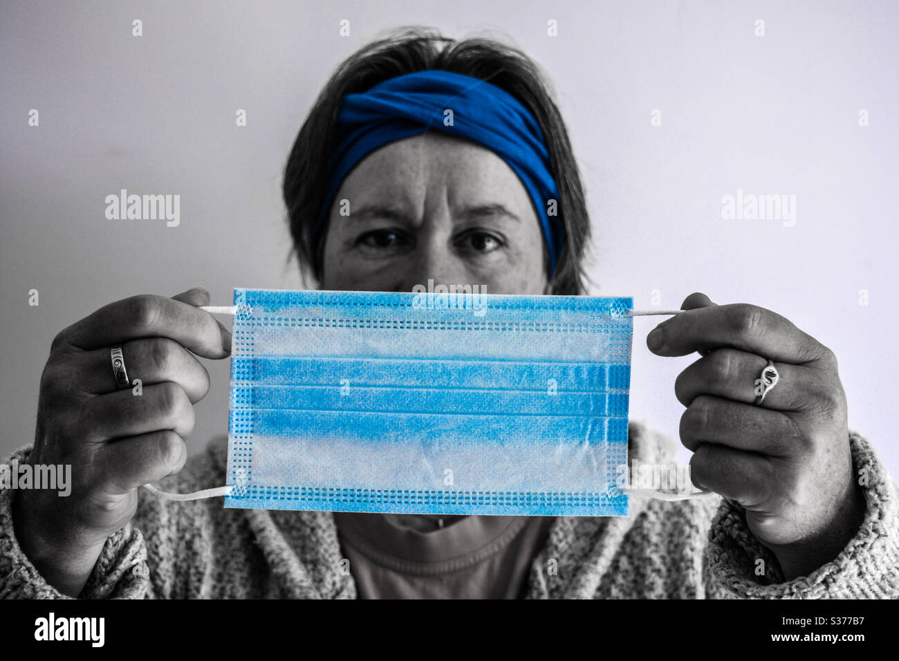 I woman holding up a 3 ply non-surgical face mask with elastic era loops. Selective focus and pop colour blue. Stock Photo