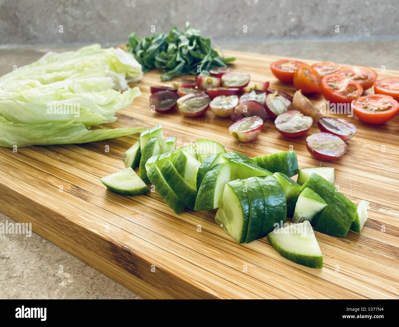 Closeup view of freshly prepared salad ingredients for dinner. Healthy red grapes, lettuce, tomatoes, cucumber. Washed and rinsed. Sliced, chopped and quartered on a wooden chopping board - Smartphone Captured Stock Image