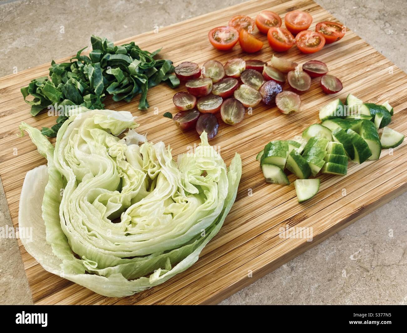Closeup view of freshly prepared salad ingredients for dinner. Healthy red grapes, lettuce, tomatoes, cucumber. Washed and rinsed. Sliced, chopped and quartered on a wooden chopping board - Smartphone Captured Stock Image