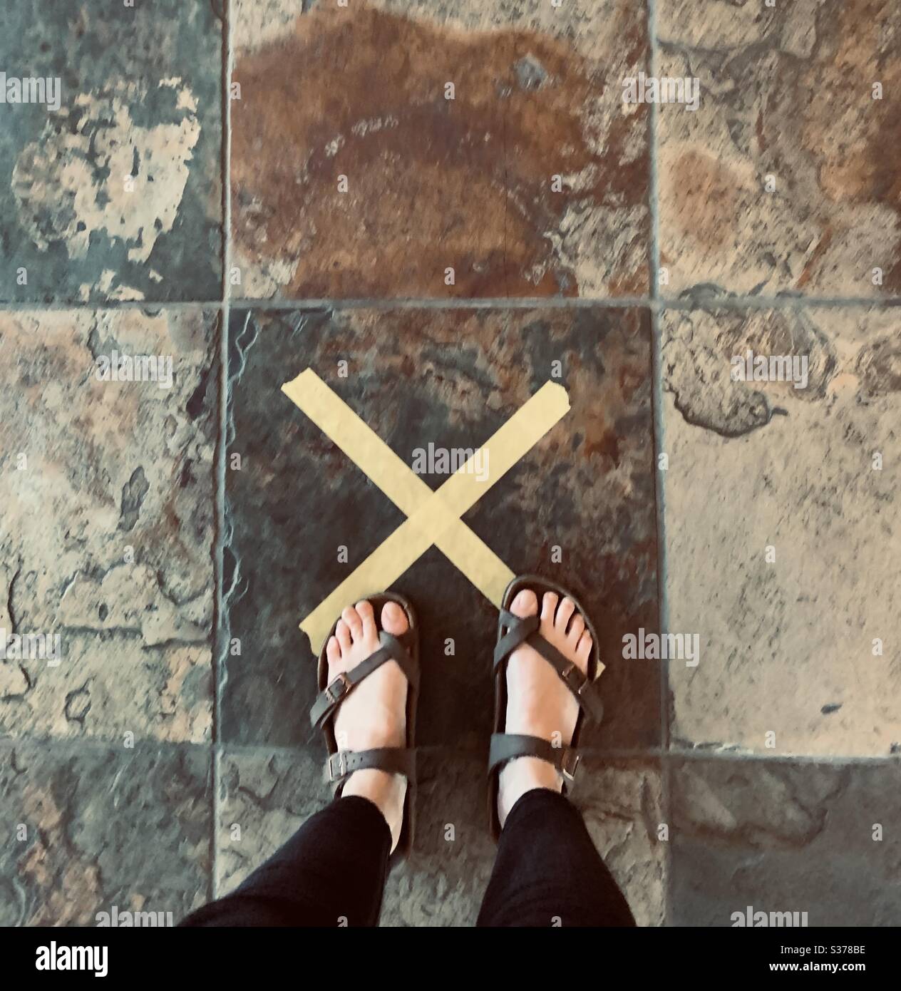 Girl standing on tile floors marked with yellow x during the coronavirus pandemic social distancing USA, America Stock Photo