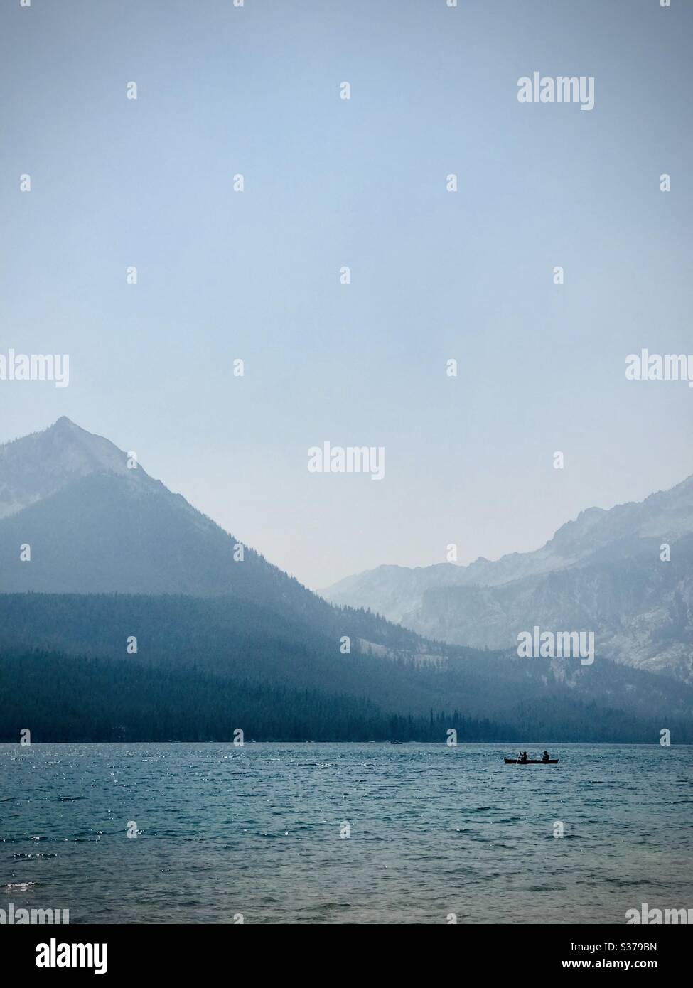 A kayaker riding across a scenic mountain lake in the northwest United States. Stock Photo
