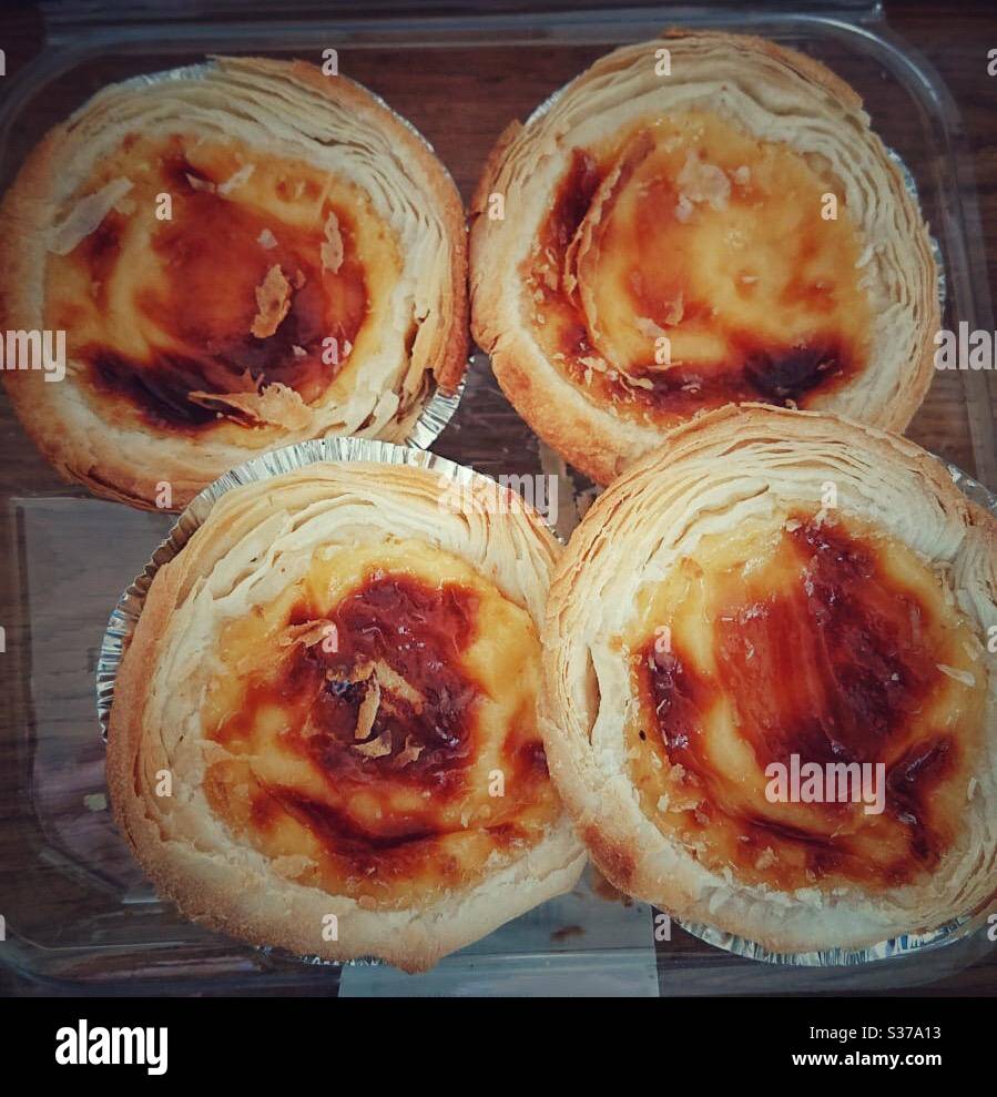 A photograph of four Portuguese egg custard tarts in a plastic box. Also known as natas. - Smartphone Captured Stock Image
