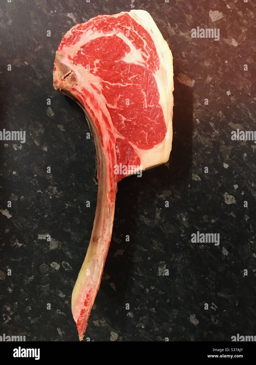 Tomahawk beef steak on a dark worktop - raw and uncooked Stock Photo