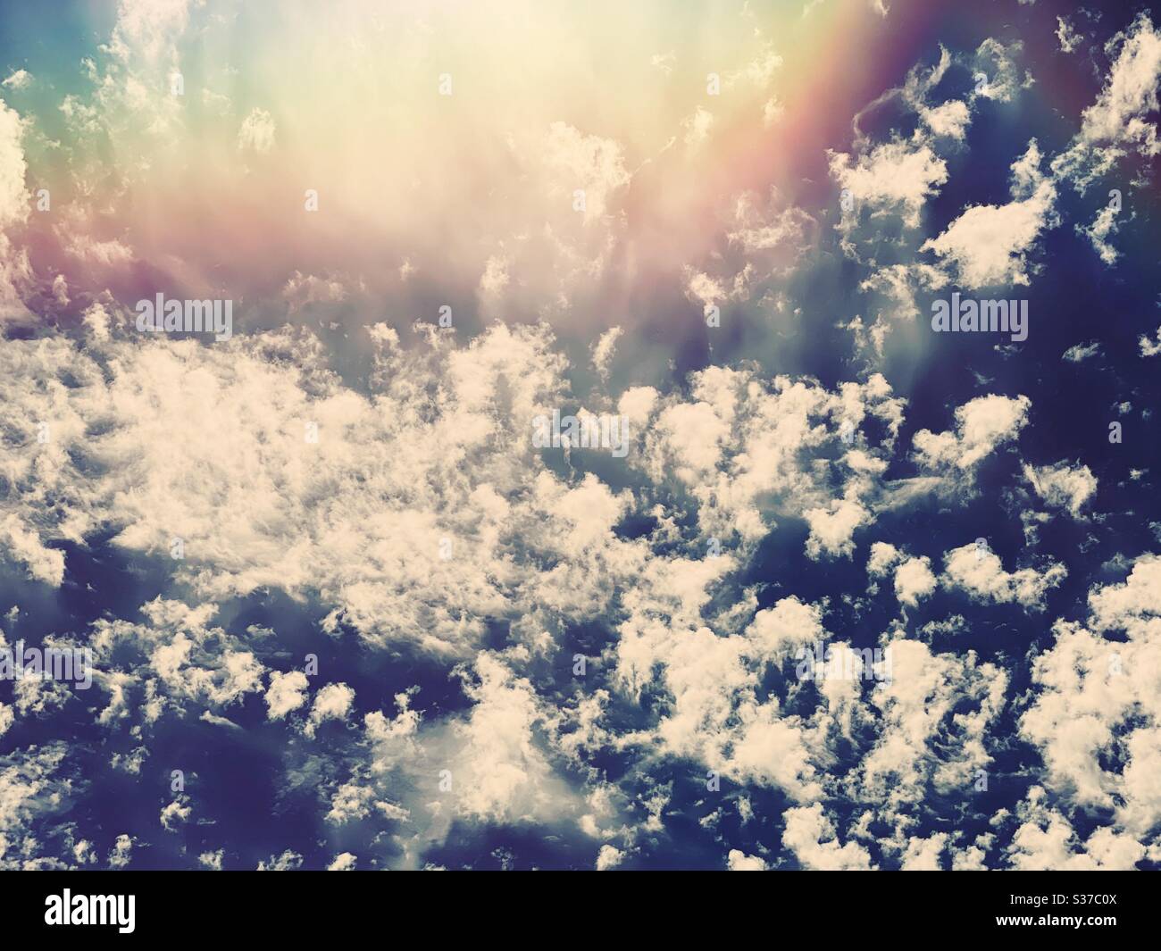 Abstract summer sky scene. White fluffy clouds are seen against a summery blue background with creative lens flare during midday sunshine. Bright light skyscape with copy space. - Smartphone Captured Stock Image