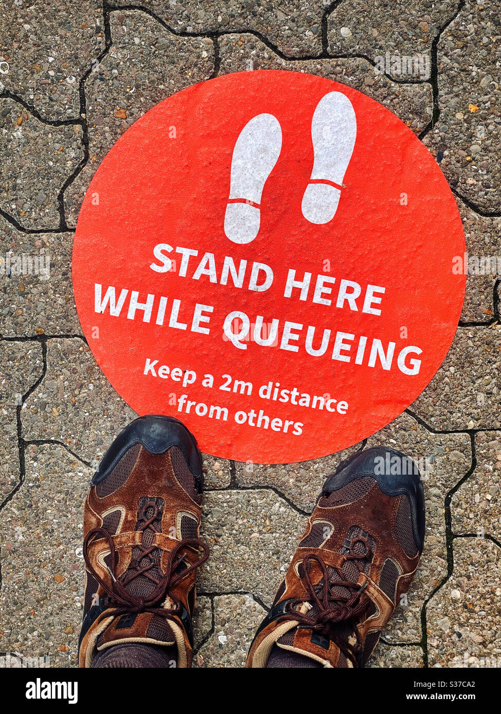 Sign on the ground “STAND HERE WHILE QUEUEING - Keep a 2m distance from others” The world is now a different place due to the Covid-19 Pandemic. Social distancing for safety. ©️ COLIN HOSKINS. - Smartphone Captured Stock Image