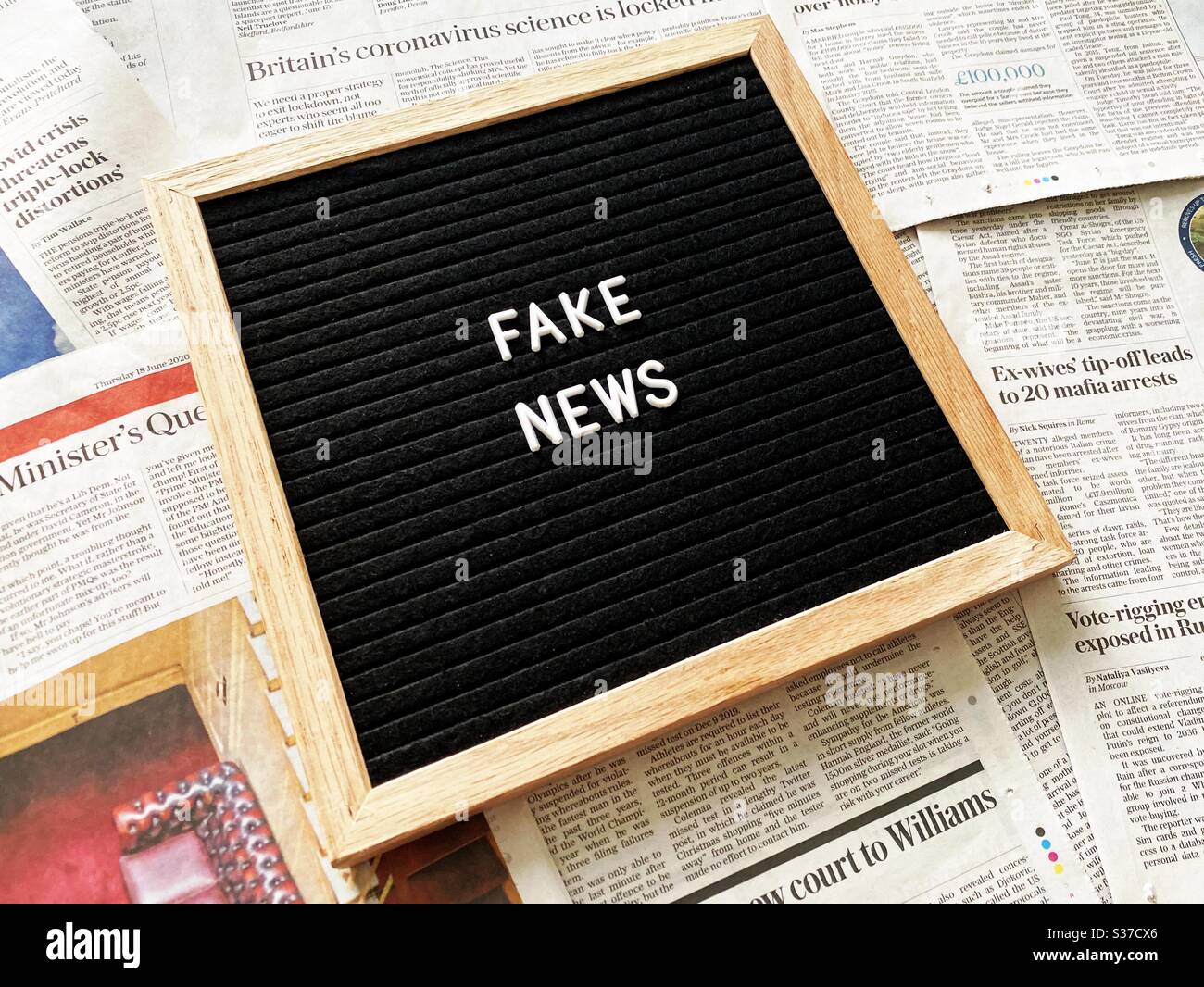 A closeup view of a black felt message board with the phrase Fake News, seen against a background of national newspaper pages. Headlines, tabloids, press and media concepts. Stock Photo