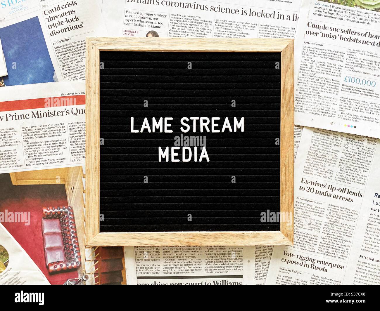 A closeup view of a black felt message board with the phrase Lame stream media, seen against a background of national newspaper pages. Headlines, tabloids, press and media concepts. Stock Photo